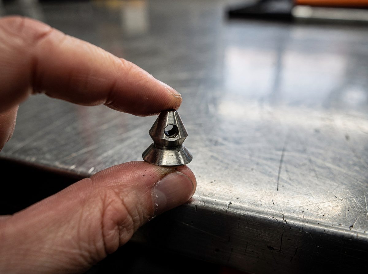 A spray nozzle tip held up for inspection on a workbench